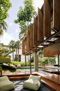 A modern residential exterior featuring wooden panels and a large swimming pool surrounded by greenery.