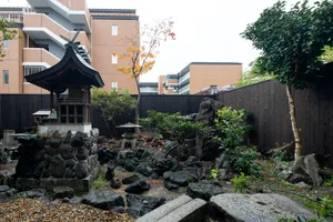A serene Japanese garden featuring a stone monument, rock formations, and greenery.