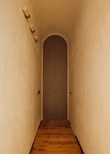 Minimalist interior featuring a hallway with wooden flooring, concrete walls, and an arched doorway.