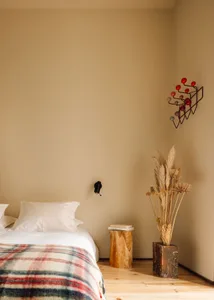 A minimalist bedroom with brown walls, a wooden bed frame, and a wooden side table with dried plants and a vase.