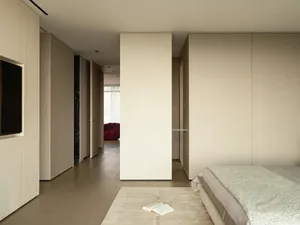 Modern bedroom with textured beige walls and wood floor, featuring a bed with beige and white bedding.