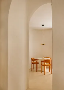 A modern dining room with a white circular table and wooden chairs, set against a white curved wall and floor.