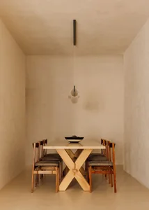 A minimalist dining room featuring a wooden and marble dining table surrounded by chairs and a modern pendant light hanging a