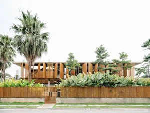 Modern residential house with wooden exterior, surrounded by plants and palm trees.