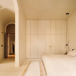 Modern minimalist bedroom with white wood flooring, cream color paneling on the wall, a single white bed with a headboard and