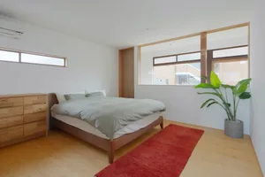 A minimalist bedroom with a bed covered in cream-colored bedding on a wooden frame, situated in a room with white walls and a