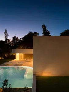 A modern residential exterior with concrete walls and a swimming pool at dusk.