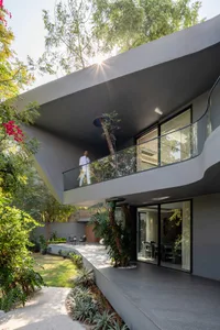 A modern residential exterior featuring concrete architecture, a balcony, and lush greenery.