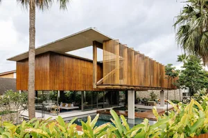 A modern residential exterior showcasing a wood and glass structure with a large overhanging roof and a pool in front.