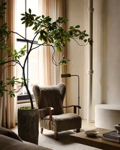 An industrial-style living room featuring a wooden armchair, woolen cushions, glass lampshade, and potted plant.