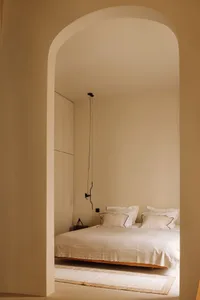 A minimalist bedroom with a white bed covered in soft textiles and wooden flooring.