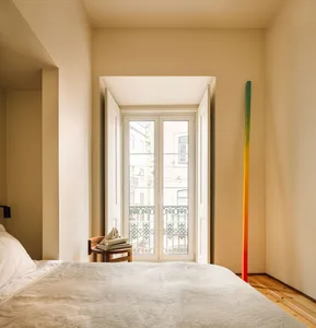 A minimalist bedroom with a bed, nightstand, and window overlooking a residential area.
