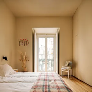 A minimalist bedroom with a wooden floor, white bedding, and a plaid blanket.