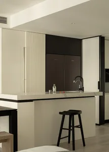 A minimalist kitchen with concrete walls, marble countertops, and black stools.