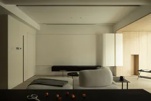 A minimalist living room with neutral-toned furniture and decor, including a corner sofa, a coffee table, and a low side tabl