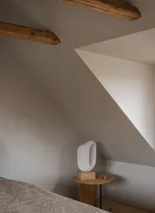 Minimalist bedroom with wooden beams and abstract sculpture on a small wooden table.