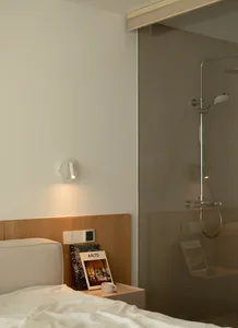 A modern minimalist bedroom with a wooden headboard and a glass-enclosed shower.