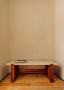 A minimalist table with a stone top and wooden frame in a plain room.