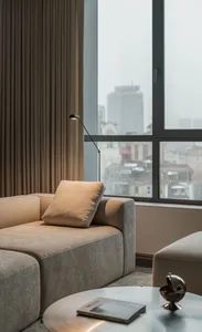 Modern minimalist living room featuring a comfortable beige fabric sofa, a sleek table lamp, and a cityscape view through lar