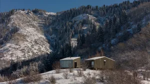 A modern house with a wooden exterior is nestled into a snowy hillside.