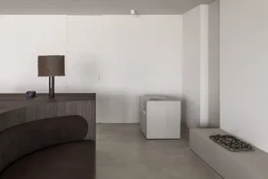 A modern minimalist interior space featuring concrete elements, a wooden sofa, a lamp, and a stone feature wall.