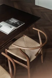 A wooden chair with a woven seat sits next to a dark wooden table with an open magazine on it, all set on a wooden-herringbon