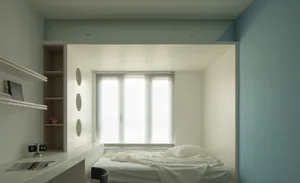 A minimalist bedroom with neutral colors featuring a bed, shelves, and a window with blinds.