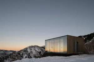 Modern house with large glass windows on a snowy hillside.