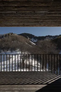 Wooden deck overlooking a snow-covered landscape with trees and hills in the background.