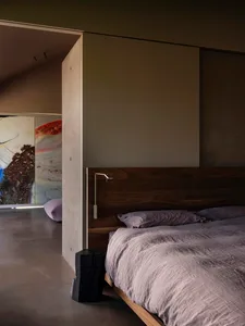 A minimalist bedroom featuring a wooden platform bed with purple bedding and a modern light fixture.