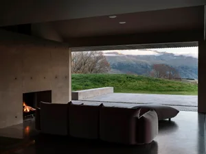 A modern living room with a concrete fireplace, plush seating, and an open view of mountains.