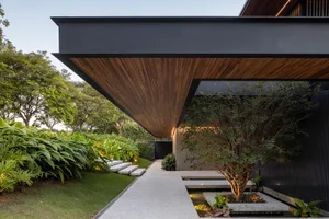 A modern exterior with wooden beams, a concrete walkway, and greenery.