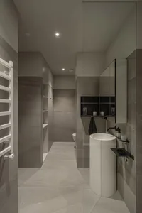 A modern minimalist bathroom with concrete tiles, featuring a sleek white pedestal sink, a large mirror, and plenty of storag