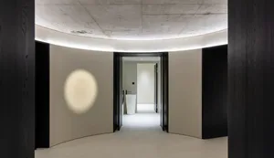 極簡室內空間，白色混凝土牆面與地板，中央擺放洗手盆。