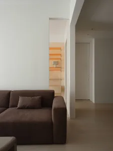 A minimalist living room with a brown fabric sofa, wooden shelves, and a neutral color palette.