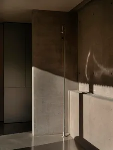A minimalist concrete bathroom with a free-standing shower head mounted on the wall.