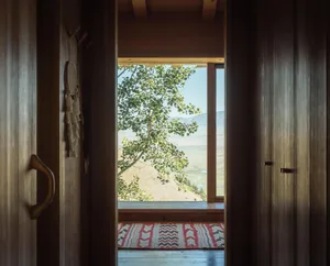 A minimalist window view of lush greenery and a scenic landscape, framed by wooden walls and floors.