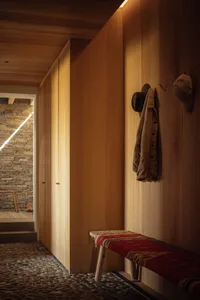 Modern entrance hall with wooden walls, wooden bench with red fabric, and stone floor.