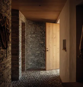 A modern entryway featuring stone and brick walls, wooden door, and pebble flooring.