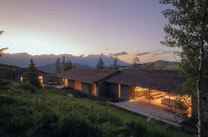 A modern residential exterior with stone walls and a wooden roof at dusk.