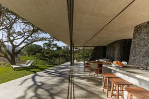 Modern residential patio featuring concrete and stone materials, with a lounge area and outdoor dining setup.