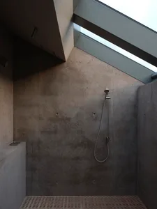 Bathroom with concrete walls, ceiling, and floor, featuring a minimalistic design with a shower head and skylight.