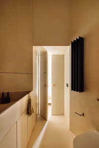 A minimalist bathroom with concrete walls and floor, featuring a sink and a toilet with a black radiator and a doorway leadin