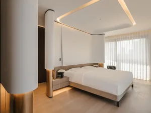 Minimalist bedroom featuring a white bed with wooden floor, white curtains, and white ceiling lighting.