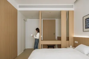 Person standing in minimalist bedroom with wood and white decor, reading a book.