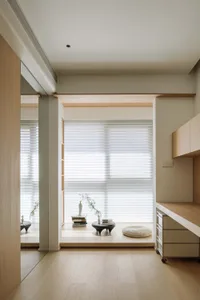 Minimalist residential interior featuring wooden floors, glass doors, and a concrete bench by a window with a vase and stack 