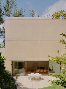 Modern house with concrete exterior, featuring a minimalist design with a large glass window and surrounding greenery.