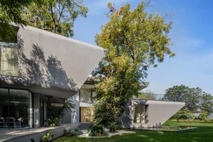 Modern house exterior with concrete walls and roof, surrounded by greenery.