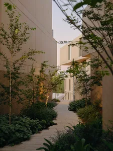 A modern indoor pathway lined with greenery, featuring concrete walls and a light source.