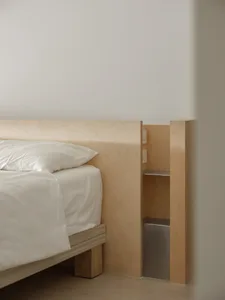 A modern minimalist bedroom with a white bed and white bedding, featuring a natural wood headboard and minimalist wooden furn